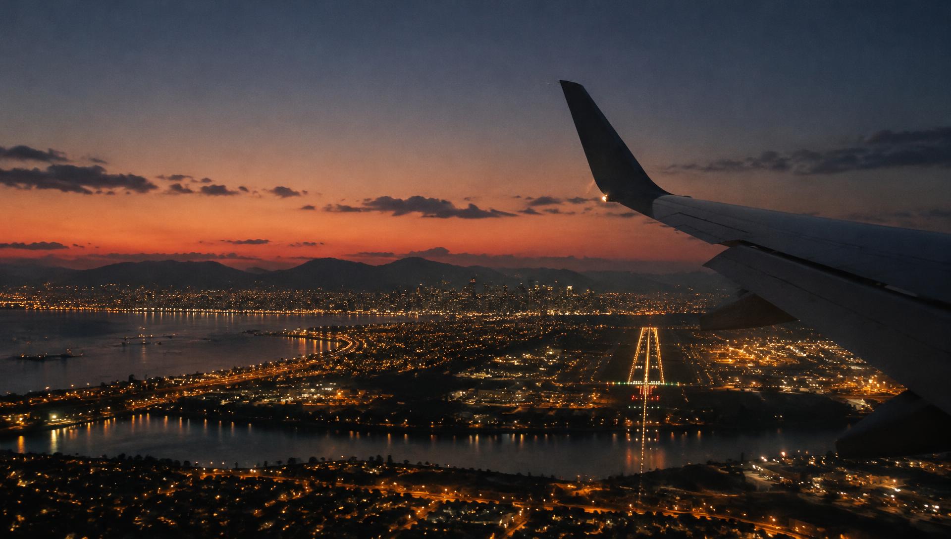 Window-seat view on final approach at dusk, city lights and runway glowing below